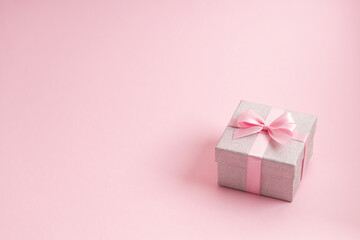 Silver glitter gift box with pink ribbon bow on pink background. Christmas, Valentine's day or birthday concept.