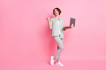 Full length photo of funky bob hairdo lady hold laptop point look empty space wear grey green suit isolated on pink background