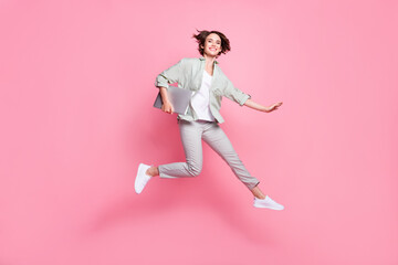 Full size photo of nice young lady jump with laptop wear grey green suit sneakers isolated on pink...