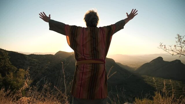 A Bible prophet or holy man raises his arms in praise on a mountain top