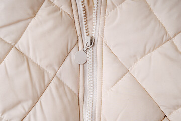 Close-up on beige puffer jacket texture with zipper. Quilted fabric background © igishevamaria