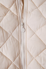 Close-up on beige puffer jacket texture with zipper. Quilted fabric background