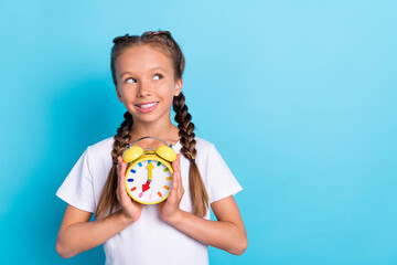 Photo of young little girl happy positive smile dream think look empty space hold timer watch isolated over blue color background