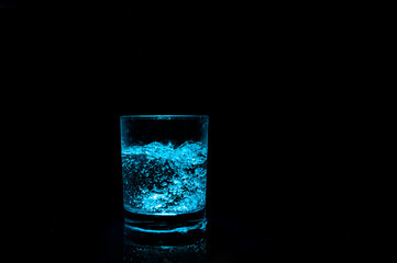glass with ice cubes and bottom illumination on dark background