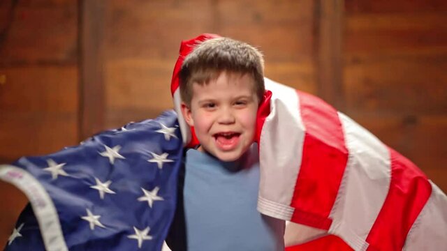 Sports fan concept. A little boy with a American flag on a wooden background. A seven-year-old kid shakes the flag of USA and is a support for the football team concept. High quality 4k footage