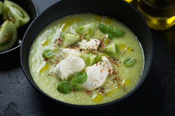 Black bowl with gazpacho soup made of green tomatoes and served with mozzarella cheese, middle closeup, studio shot