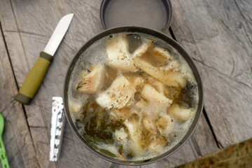 Fish soup in a metal plate on a wooden background. Cooking food on a tourist burner. Traditional food angler or tourist. 