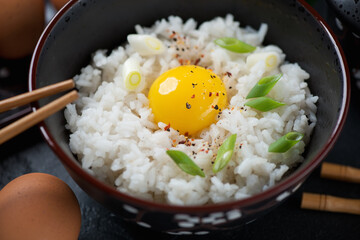 Close-up of tamago kake gohan in a black bowl or japanese warm rice mixed with a raw chicken egg