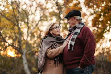 Elderly man lovingly looks at his elegant pensioner, hugs and enjoys her beauty, senior married couple dancing in autumn park, celebrating anniversary, affection