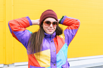 Happy young girl in a knitted hat near the yellow wall. Hipster in sunglasses and bright clothes....