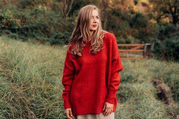 A beautiful blonde with long hair in a red warm sweater is walking in the autumn landscape.