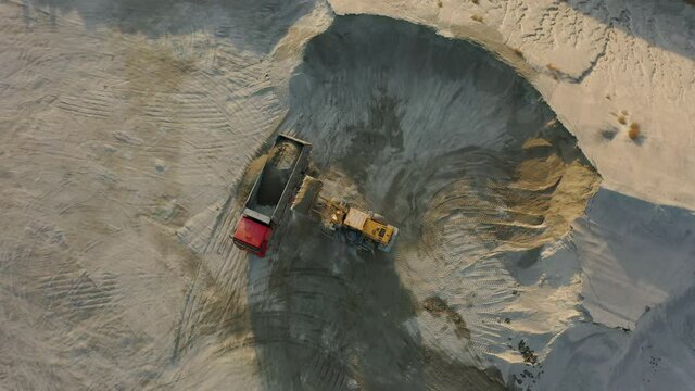 Front loader loading crushed stone into dump truck in quarry, aerial top down view. Excavator working on plant for production of building materials