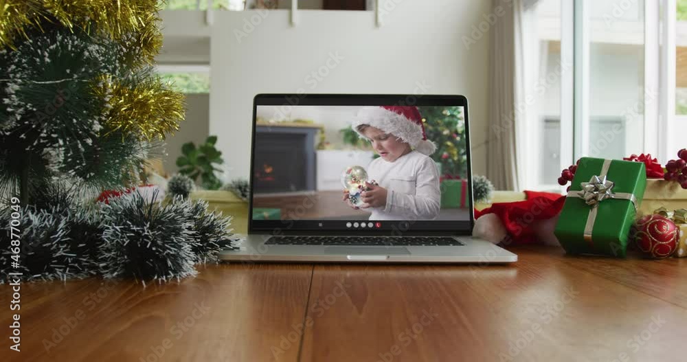 Wall mural Caucasian boy with santa hat playing with snow globe on christmas video call on laptop