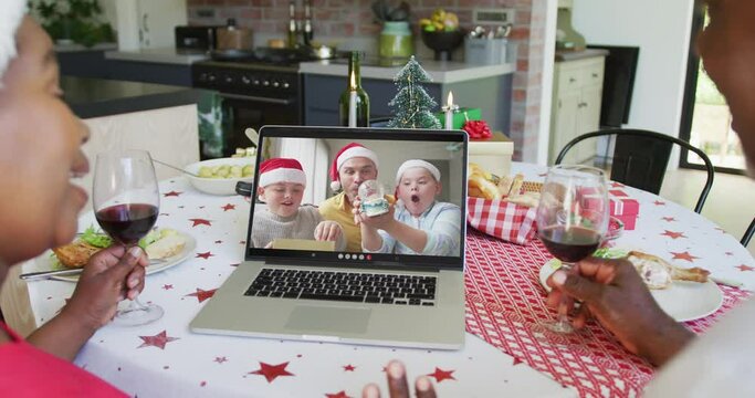 African american couple with wine using laptop for christmas video call with family on screen