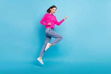 Fototapeta na wymiar Photo of charming lucky young woman dressed pink sweater jumping high rising fists isolated blue color background