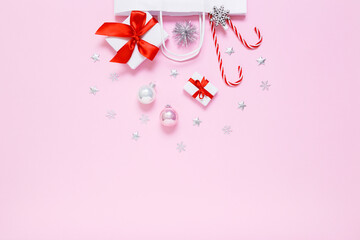 Christmas, New Year composition. White paper bag with presents, sweet candy canes, holiday decorations, pink and silver balls, silver glitter confetti stars on pastel pink background. Flat lay