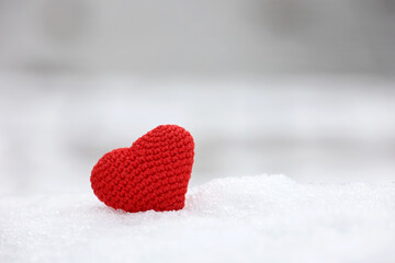 Red knitted heart in the snow with blurred nature background. Valentine's card, symbol of love, romantic event at winter, Christmas celebration