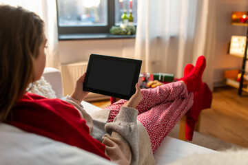 christmas, winter holidays and leisure concept - young woman with tablet pc computer resting feet on table at home