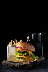 burger with a double cutlet and vegetables on a dark background, French fries and a drink, vertically