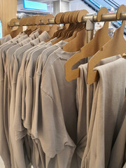 Gender neutral style clothes hang on eco-friendly cardboard paper hangers on rack in casual clothes store in trendy pastel tones and nude colors. Gender free clothing concept. Selective focus