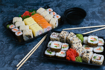Sushi sets in plastic packaging, food delivery concept during quarantine covid 19. Rolls with salmon, eel, red fish, cheese, nori, sesame and rice, wasabi, ginger and soy sauce on a dark background