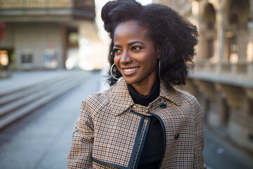 Beautiful African American young woman with afro and large hoop earrings in a stylish coat,...