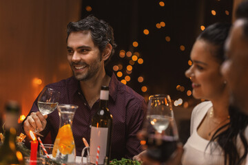 holidays and celebration concept - happy man having christmas dinner with friends and drinking wine at home