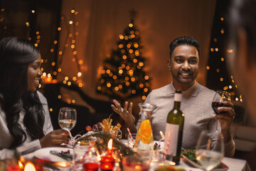 holidays, party and celebration concept - multiethnic group of happy friends having christmas dinner at home and drinking wine