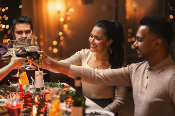 holidays, party and celebration concept - multiethnic group of happy friends having christmas dinner at home and drinking wine