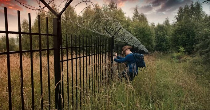 Man runs to the fence with barbed wire and climbs on it. Evening sunset. The concept of illegal border crossing, penetration into a protected object and unlawful migration