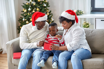 family, winter holidays and people concept - happy african american mother, father and little son opening gift box at home on christmas