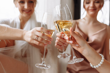 Morning of bride. Gorgeous bride with best bridesmaids are holding glasses and drinking champagne in hotel bathroom near the window. Sexy bridesmaids in exciting negligee. Wedding morning details