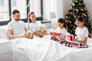 family, winter holidays and people concept - happy mother, father and two daughters in pajamas with...