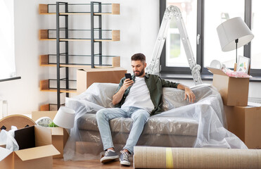 moving, people and real estate concept - man with smartphone and boxes at new home