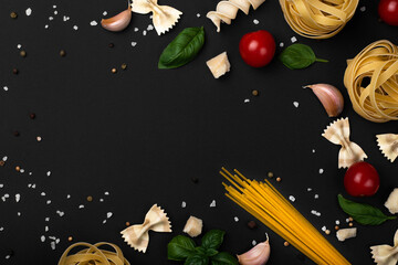 Food ingredients for italian pasta, spaghetti, basil leaves, cherry tomatoes, garlic, parmesan, chili pepper and various pasta on black wooden background.Copy space of your text.