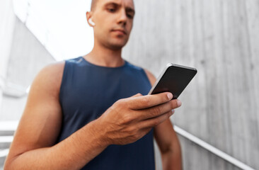 fitness, sport and technology concept - young athlete man with earphones and smartphone listening to music outdoors