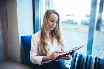 Confident woman with book near window in cafeteria