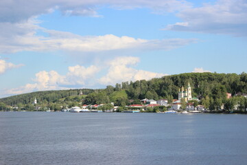 Fototapeta premium The city of Ples on the banks of the Volga River - view from the ship. green hills, houses, a church with domes and a bell tower.
