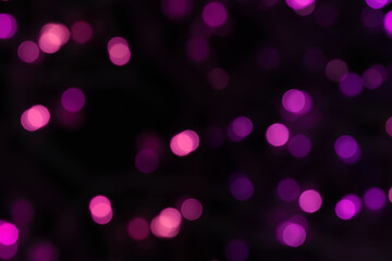 Defocused bokeh light on black background, an abstract naturally blurred backdrop for Christmas eve or birthday party. Festive light texture. Purple and pink garland blurred. Overlay effect for design