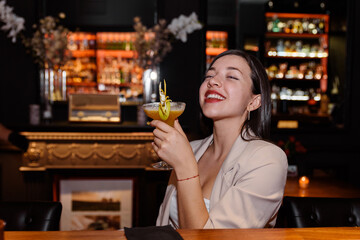 happy young woman drinks a cocktail at a bar counter