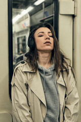 A girl in a beige trench coat rides in a subway car