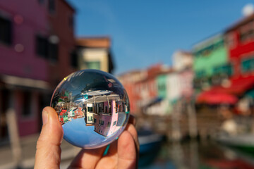Hand holding glass sphere in front of colorful houses