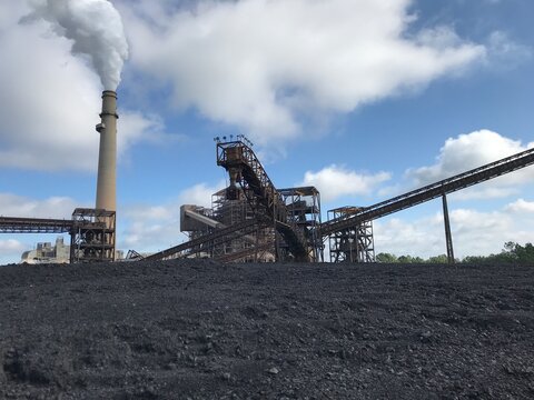 A pile of coal, a thermal power plant and a chimney that produces steam.