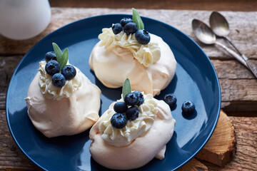 Mini Pavlova Cake with blueberries on a blue plate and a wooden board. Wooden background, side view