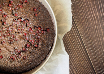 there is a round vegan brownie with red currants on parchment paper. after the oven. top view. gluten-free, lactose-free pastries