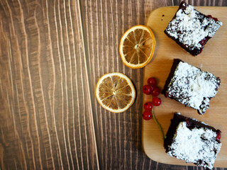 three pieces of gluten-free brownie with red currants lie on a wooden board with slices of dried lemon. gluten- and lactose-free cakes. top view