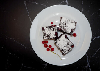three pieces of gluten-free cakes with red currants, sprinkled with powdered sugar, lie on a white plate on a black marble table. gluten-free and lactose-free cakes. homemade cakes with a diet