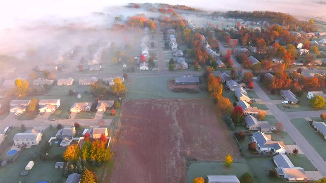 Beautiful frosty Fall neighborhood at dawn, with colorful trees and a little fog, aerial view.
