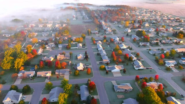 Beautiful frosty Fall neighborhood at dawn, with colorful trees and a little fog, aerial view.

