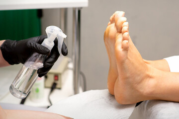 Pedicure master disinfects the feet of woman with the preparation decontamination in beauty salon